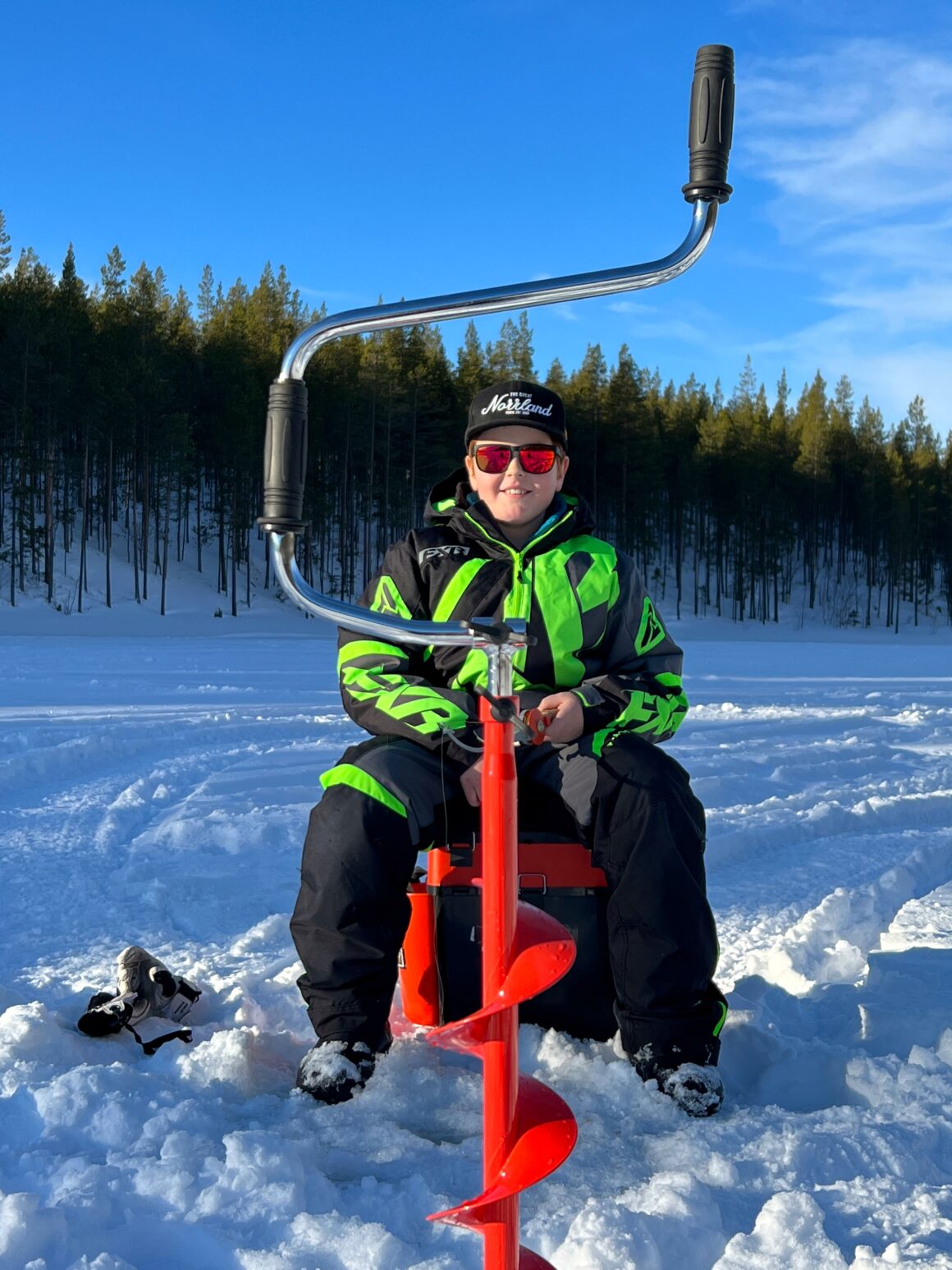Isfiske vid Järpbäcksdammen i Vemdalen. Felix Fredin fiskar med en röd 
isborr i förgrunden på bilden. 